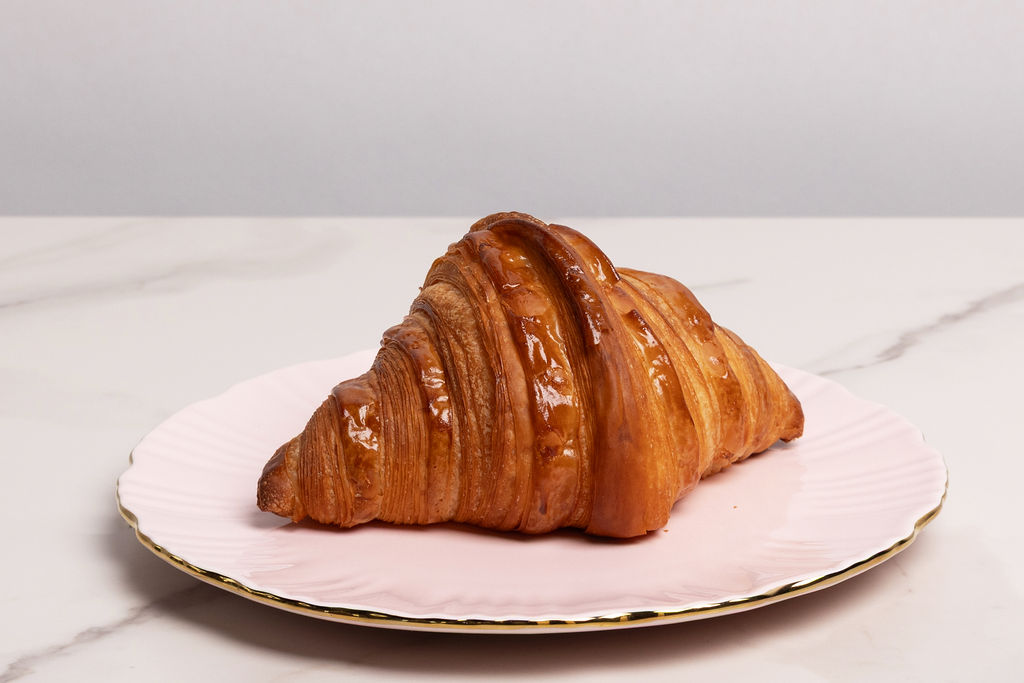 A single croissant on a pink scalloped plate