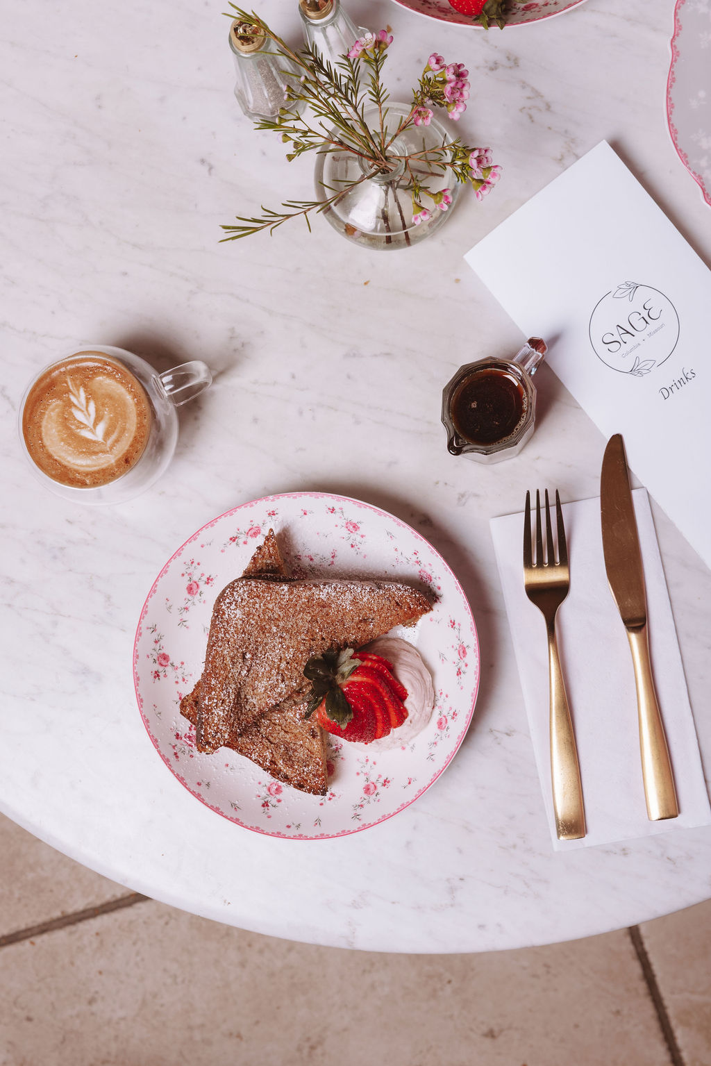 Overhead flat-lay of French toast on a floral plate with latte and Sage menu